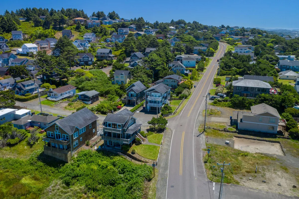 A peaceful exterior scene featuring houses perched on a hillside amid a tree-covered landscape, with a curved road leading into the community. The environment is quiet and inviting, ideal for walks or outdoor exploration with pets.
