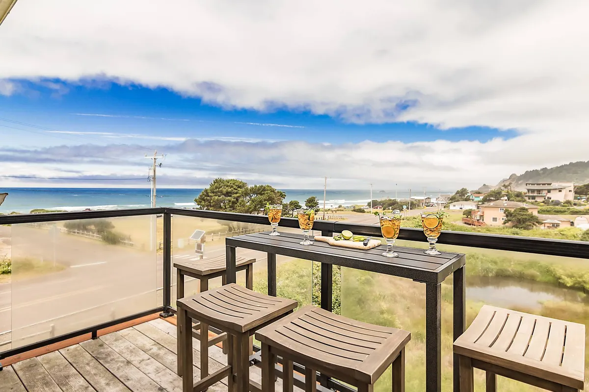 An inviting exterior scene with a bar table set with cocktails, overlooking the ocean. This space is perfect for socializing, enjoying a morning coffee or a sunset drink, all while being immersed in stunning natural views.