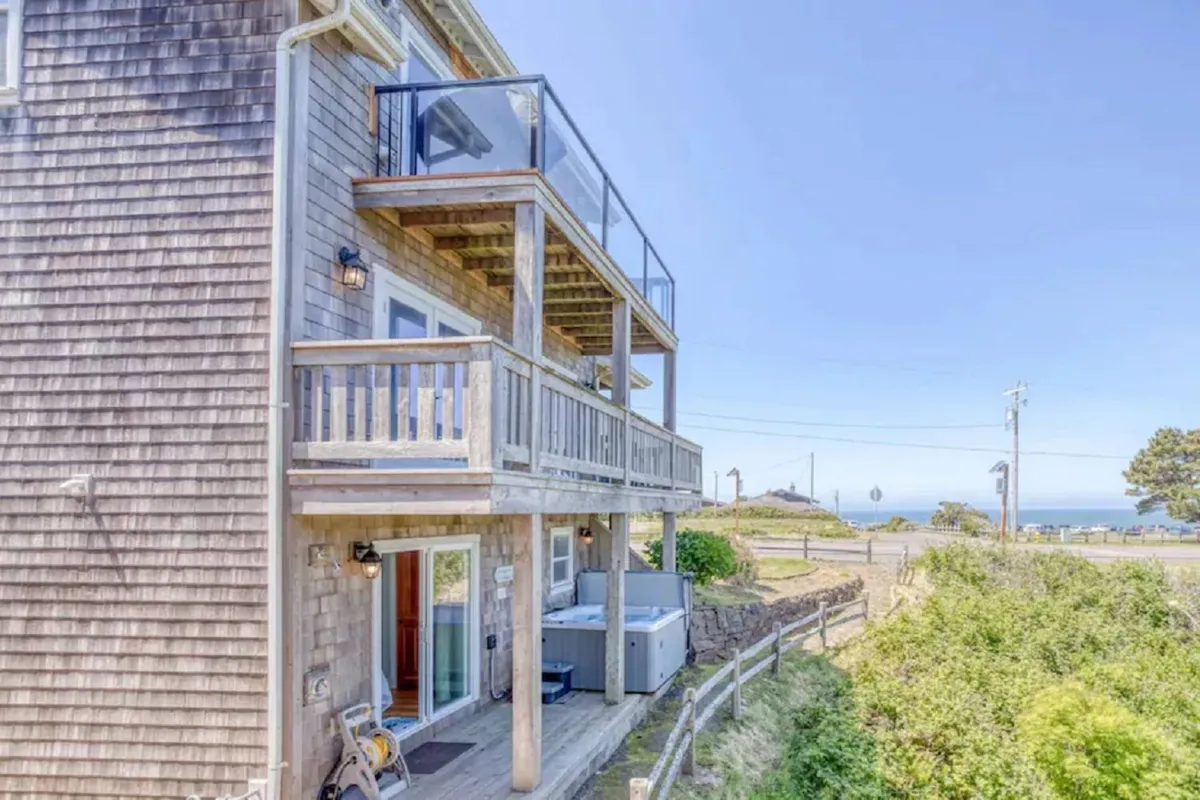 This exterior shot captures the second-floor balcony featuring a hot tub with sweeping views of the ocean. The scene is tranquil, with the hot tub and balcony suggesting spaces for relaxation and group gatherings as the sun sets over the water.