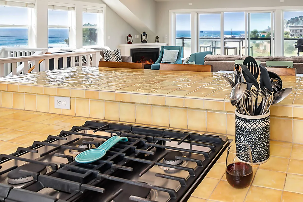 A cheerful, fully stocked kitchen with a central island, gas stove, ample counter space, and a view of the ocean beyond. The space is bright and functional, inviting guests to prepare coastal-inspired meals or gather for casual breakfasts.