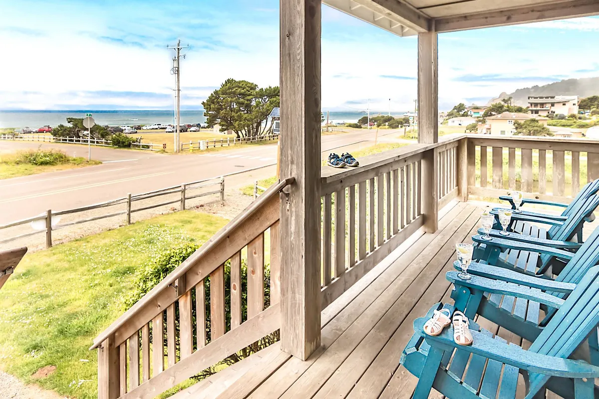 A cozy outdoor seating area with blue chairs arranged to overlook the ocean, bordered by lush roadside greenery. The spot is perfect for relaxing and soaking in the view, with plenty of space for a pet to lounge nearby.