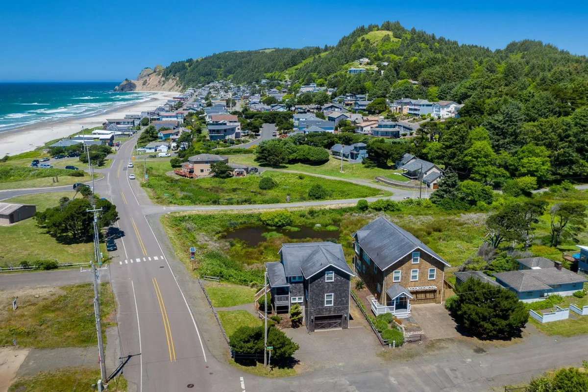 A wide-angle exterior shot showcasing a sandy beach bordered by a row of houses and lush roadside greenery. The scene captures the proximity of residential homes to the coastline, suggesting easy beach access and opportunities for a variety of outdoor activities. The relaxed mood and open expanse invite thoughts of family games, walks, and playtime with pets.