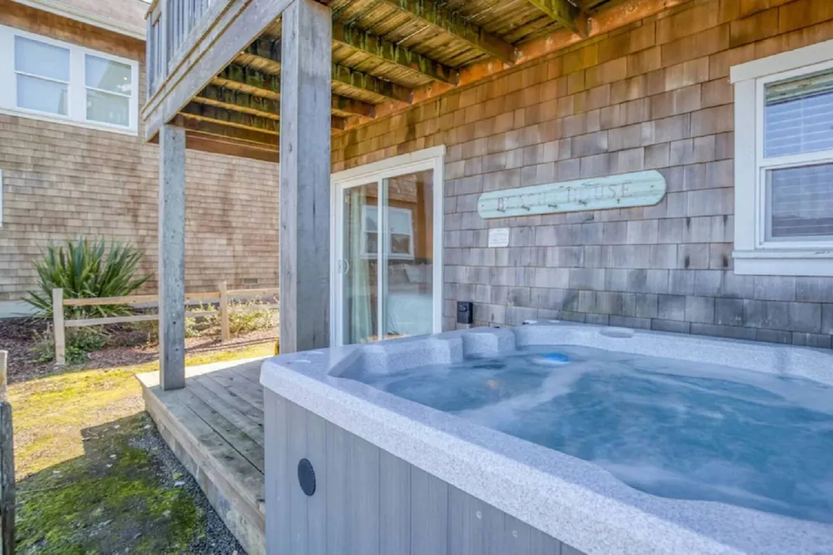 The image showcases a tranquil hot tub on a wooden deck with shingle siding, providing a comfortable setting overlooking the natural landscape. The scene captures the soft glow of sunset, evoking a sense of serenity and privacy.