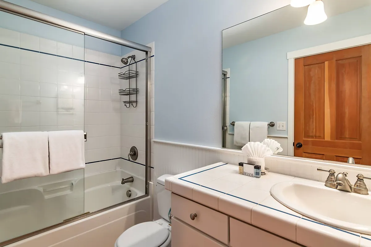 A spa-like bathroom featuring a glass shower enclosure, fluffy white towels, a wooden door, and a clean countertop accented by calming neutral tones. The overall ambiance is soothing and inviting, ideal for a refreshing start or peaceful wind-down.
